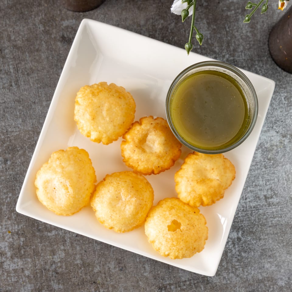 Golden-fried pani puri shells arranged on a white rectangular plate with a bowl of green pani.