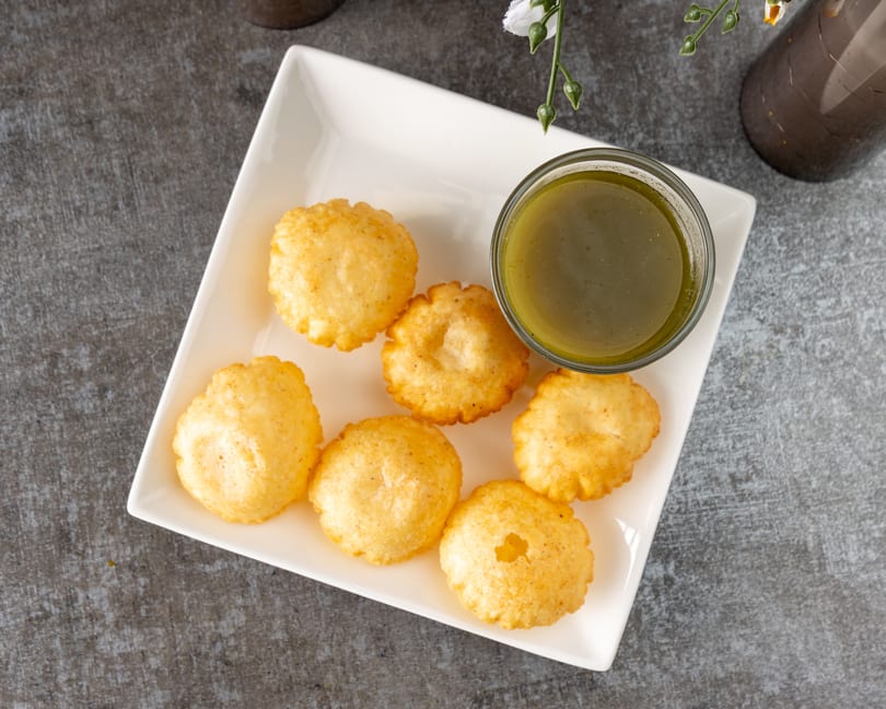 Golden-fried pani puri shells arranged on a white rectangular plate with a bowl of green pani.