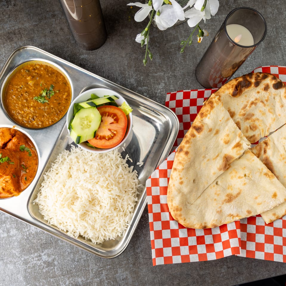 Indian thali with butter chicken, dal makhani, rice, salad, and naan bread on a checkered napkin.