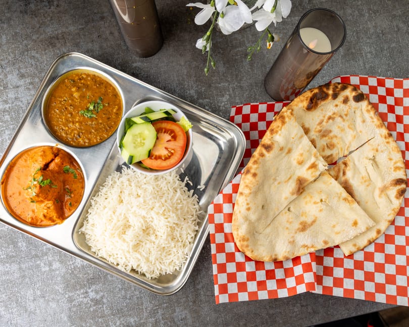 Indian thali with butter chicken, dal makhani, rice, salad, and naan bread on a checkered napkin.