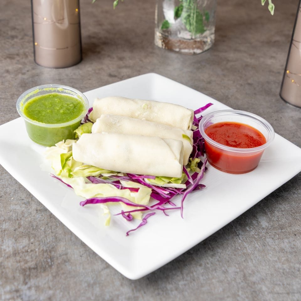 Three spring rolls on a bed of shredded cabbage, with green and red dipping sauces.