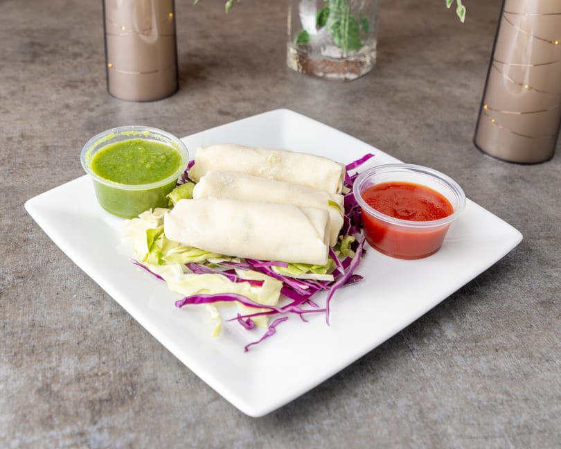 Three spring rolls on a bed of shredded cabbage, with green and red dipping sauces.