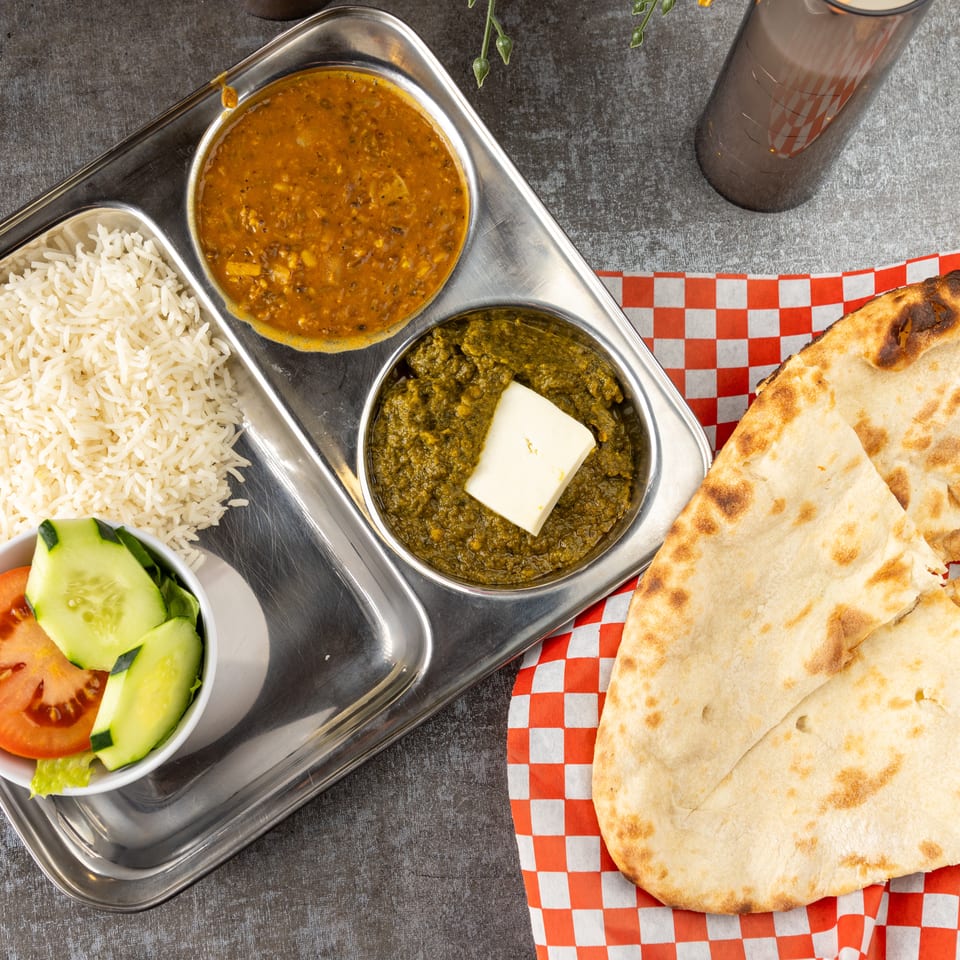 Overhead view of an Indian thali with rice, dal, saag paneer, salad, and naan bread.