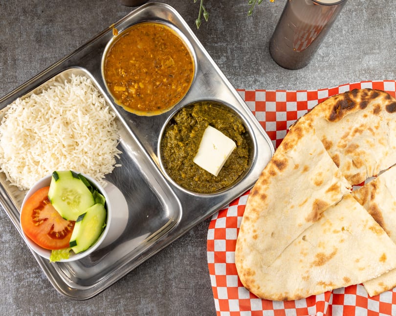 Overhead view of an Indian thali with rice, dal, saag paneer, salad, and naan bread.