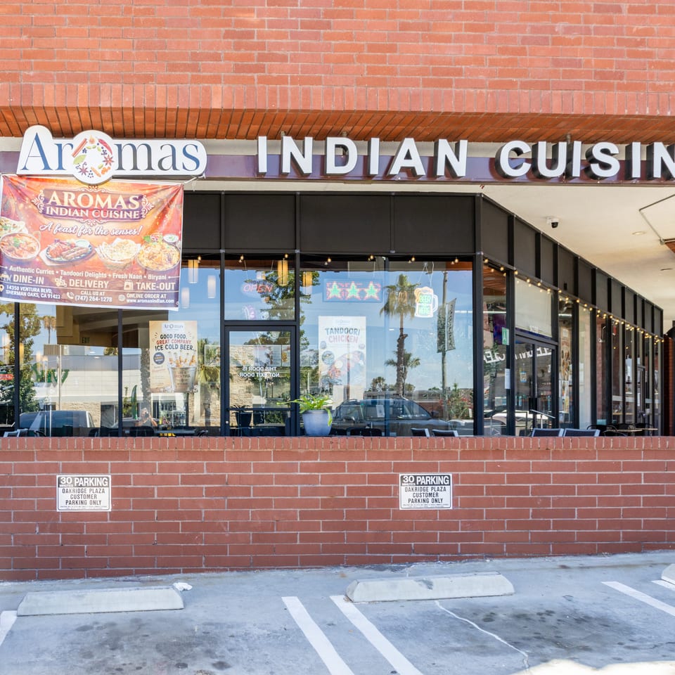Exterior view of Aromas Indian Cuisine restaurant with a large banner advertising their menu and services.