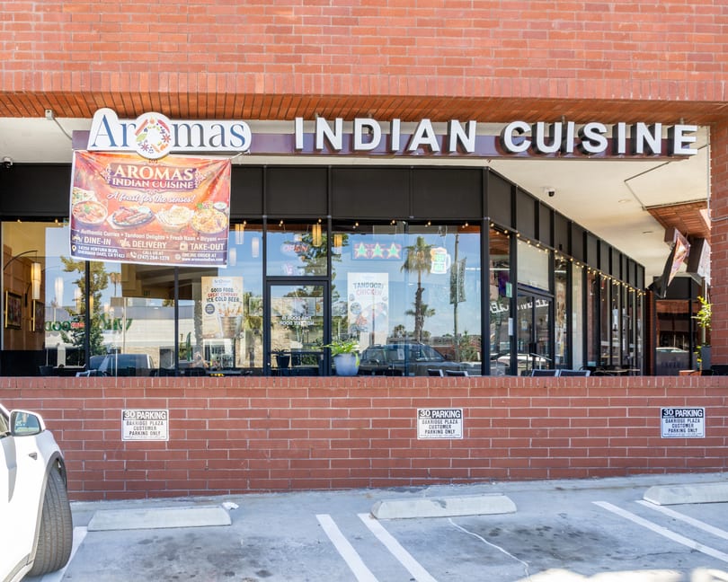 Exterior view of Aromas Indian Cuisine restaurant with a large banner advertising their menu and services.