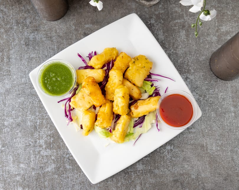 Golden fried paneer pakora on a bed of lettuce with green chutney and red sauce.