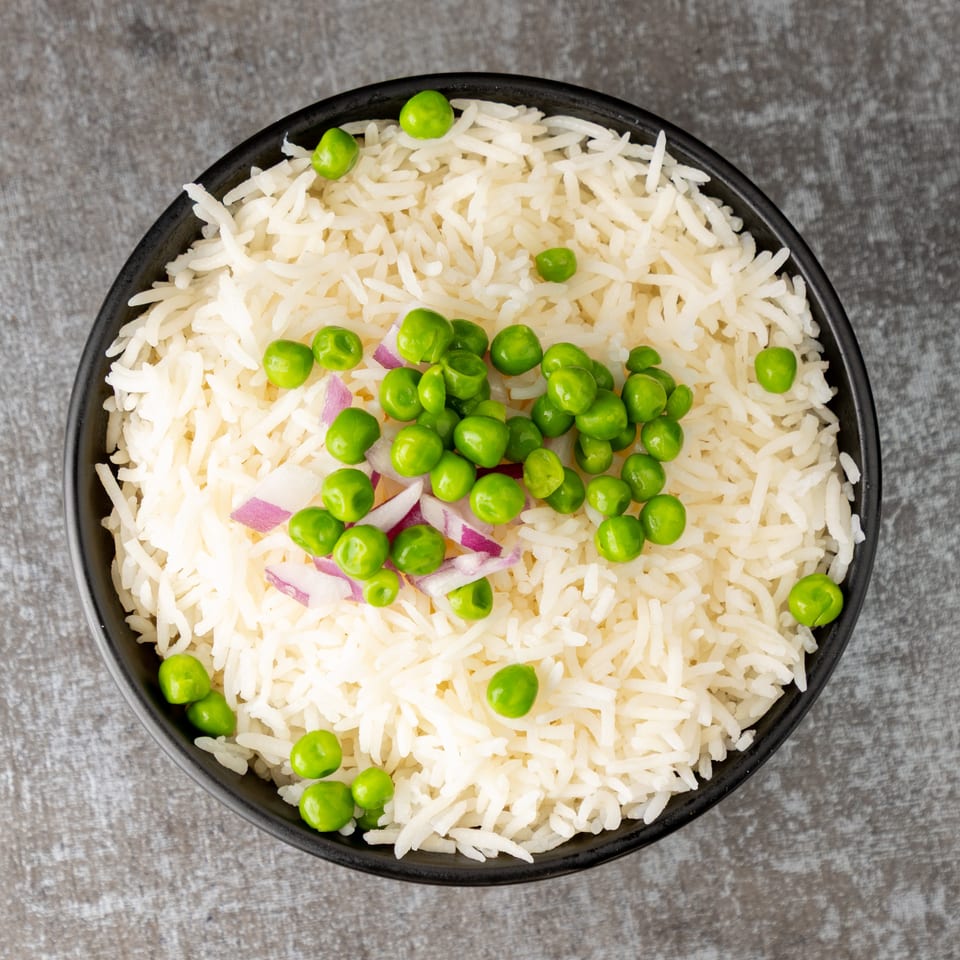 Overhead view of a black bowl filled with white rice, green peas, and red onion.