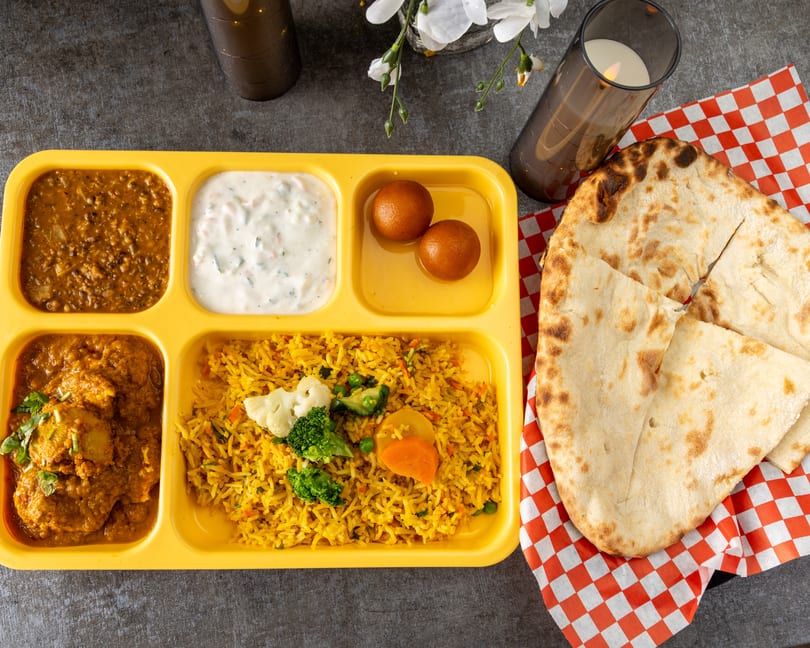 Indian thali with dal, raita, gulab jamun, chicken curry, vegetable biryani, and naan.