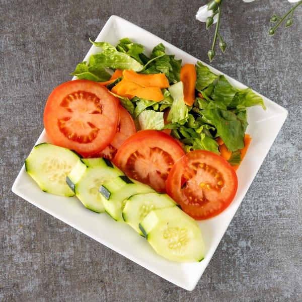 Fresh garden salad with sliced tomatoes, cucumbers, lettuce, and carrots on a white rectangular plate.
