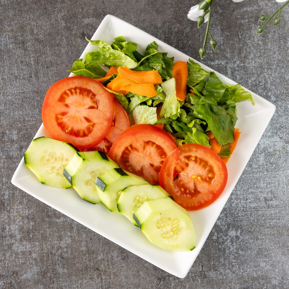 Fresh garden salad with sliced tomatoes, cucumbers, lettuce, and carrots on a white rectangular plate.