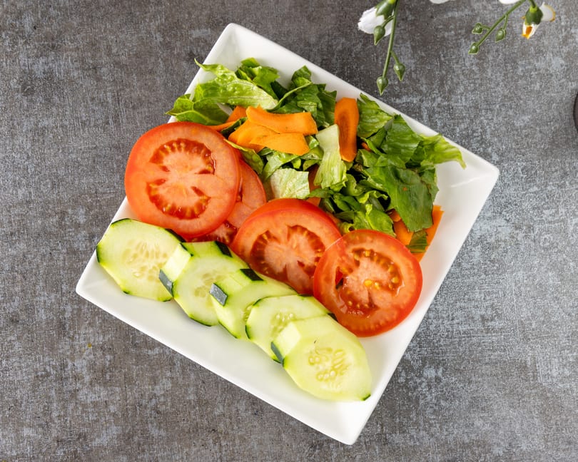 Fresh garden salad with sliced tomatoes, cucumbers, lettuce, and carrots on a white rectangular plate.
