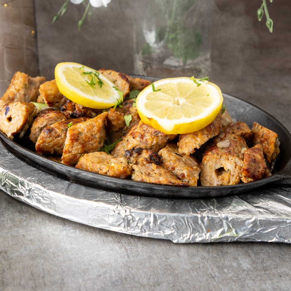 Sizzling chicken tikka with lemon slices and cilantro on a black platter, with green chutney.