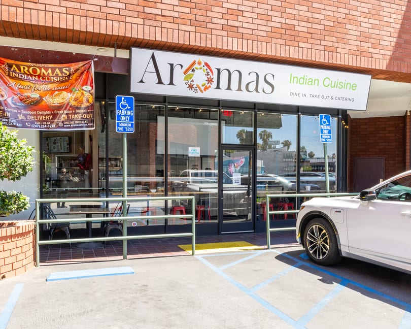 Aromas Indian Cuisine restaurant exterior with a banner, outdoor seating, and a white car parked.