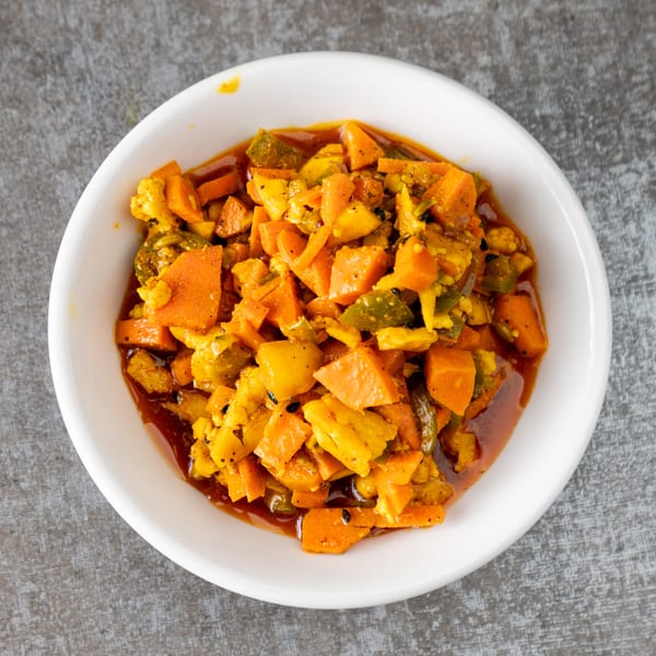 A white bowl filled with vibrant orange and green pickled vegetables in a rich, dark sauce.