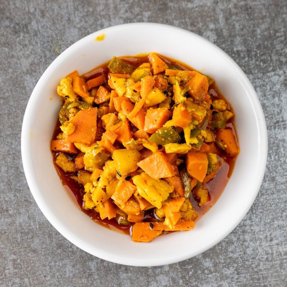 A white bowl filled with vibrant orange and green pickled vegetables in a rich, dark sauce.