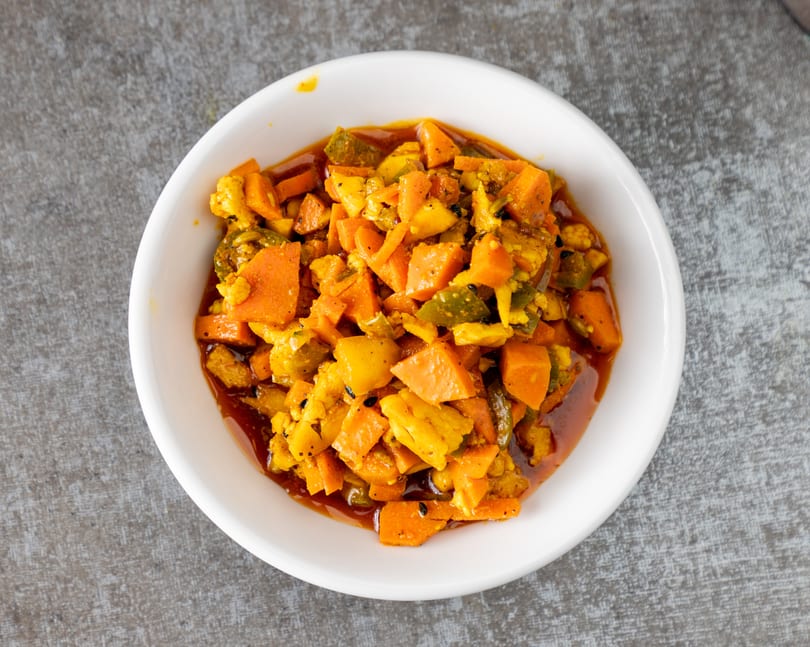 A white bowl filled with vibrant orange and green pickled vegetables in a rich, dark sauce.