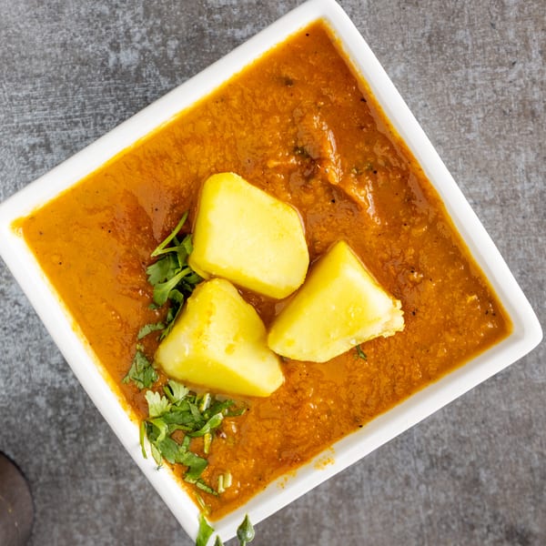 Overhead view of a white rectangular bowl filled with orange curry, topped with potatoes and cilantro.