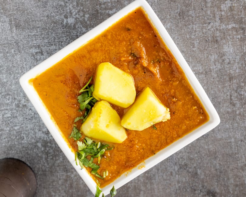 Overhead view of a white rectangular bowl filled with orange curry, topped with three potato chunks and cilantro.