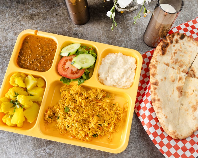 Indian thali with dal, rice, cauliflower, salad, raita, and naan on a yellow tray.