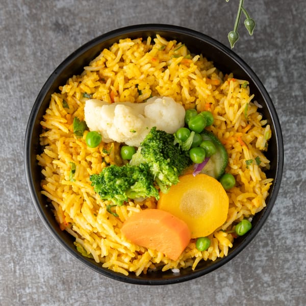 Overhead view of a black bowl filled with yellow rice and mixed vegetables.