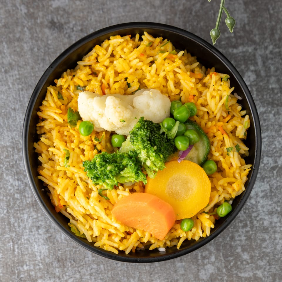 Overhead view of a black bowl filled with yellow rice and mixed vegetables.