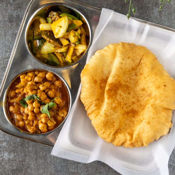 A metal tray with two bowls of Indian food and a large piece of fried bread.