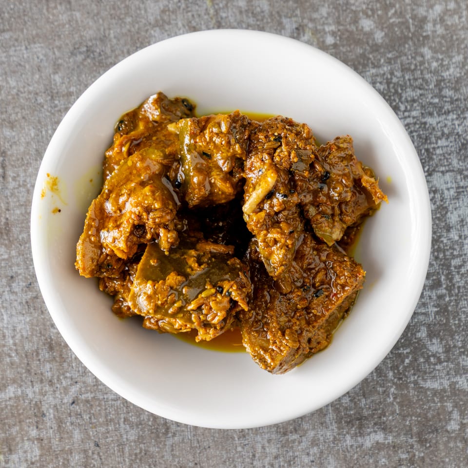 A white bowl filled with a rich, dark orange pickle, featuring visible spices and chunks of fruit.