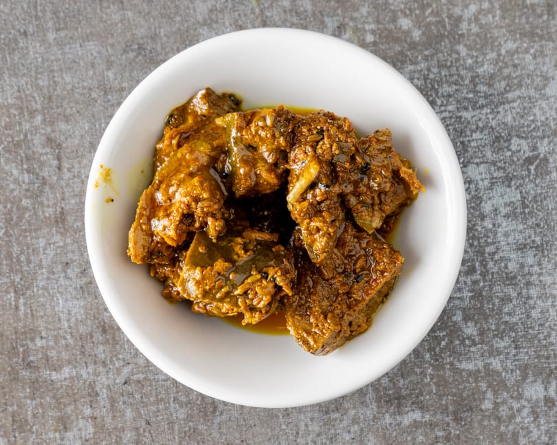 A white bowl filled with a rich, dark orange pickle, featuring visible spices and chunks of fruit.