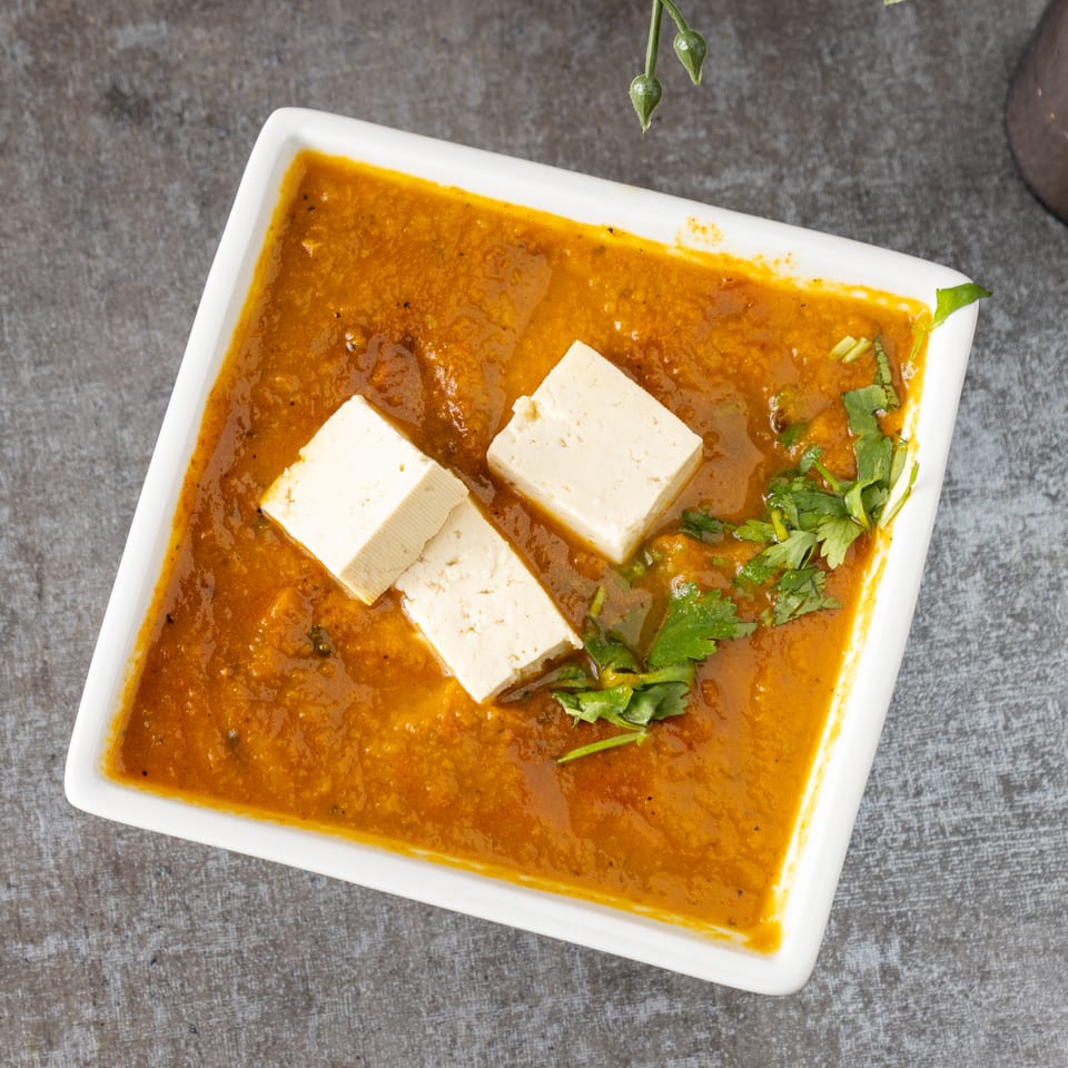 Overhead view of a white rectangular dish filled with orange curry, topped with paneer and cilantro.