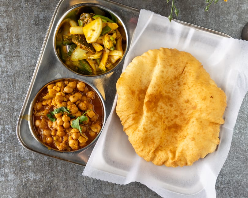 A metal tray with two bowls of Indian food and a large piece of fried bread.