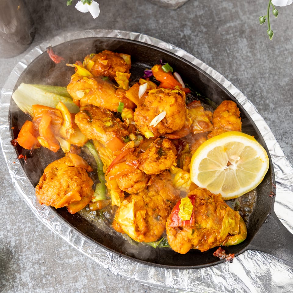 Sizzling chicken tikka with vegetables and a lemon slice on a hot plate.