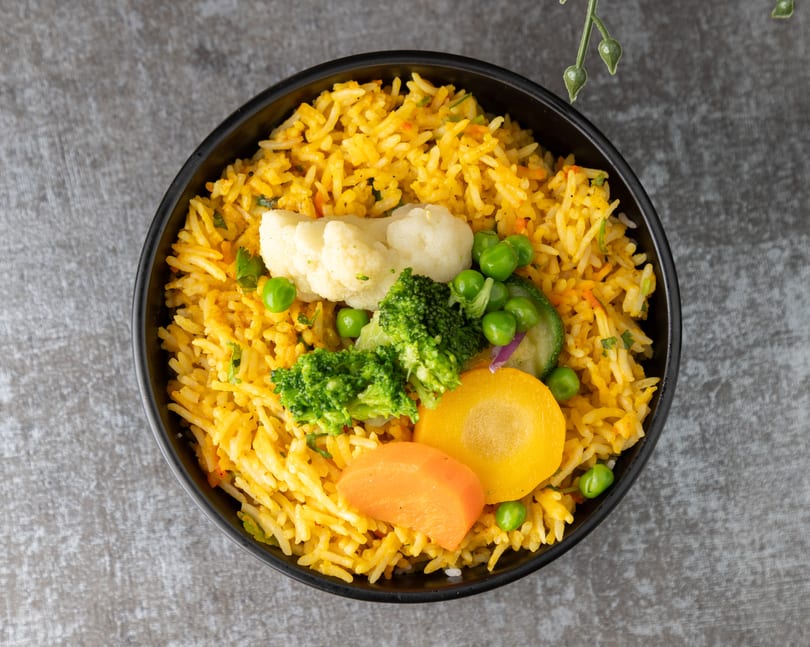 Overhead view of a black bowl filled with yellow rice and mixed vegetables.