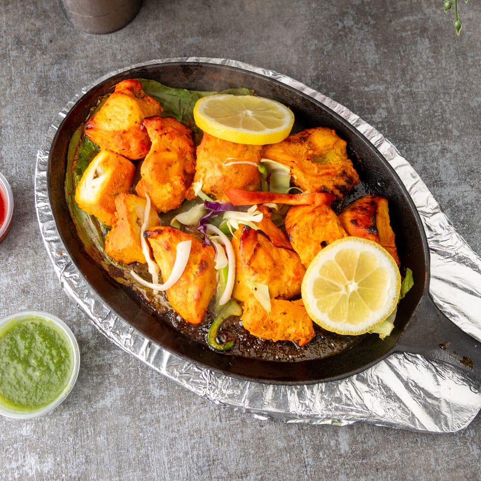 Sizzling chicken tikka with lemon slices, onions, and bell peppers in a cast iron pan.