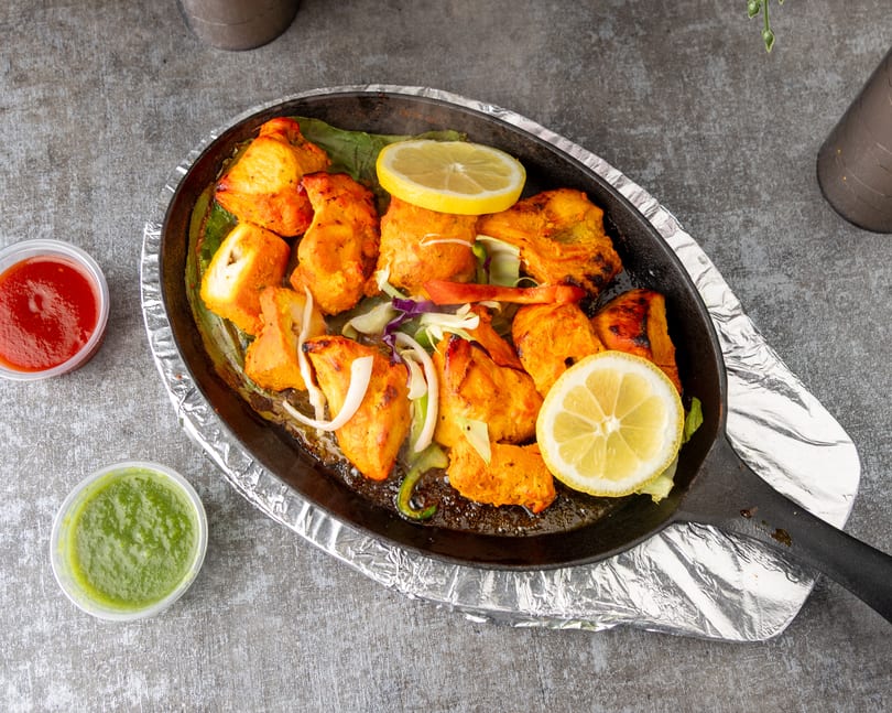 Sizzling chicken tikka with lemon slices, onions, and bell peppers in a cast iron pan.