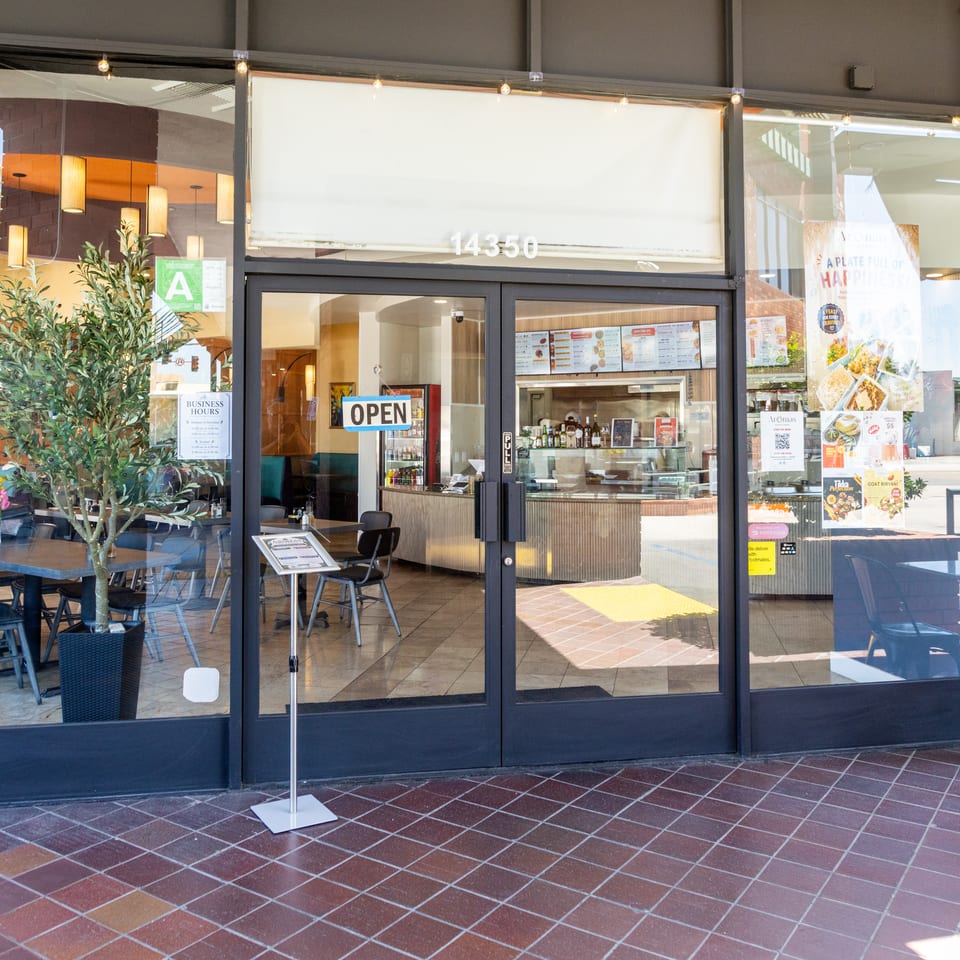 The storefront of Aromas restaurant, with an "OPEN" sign on the glass door and outdoor seating.