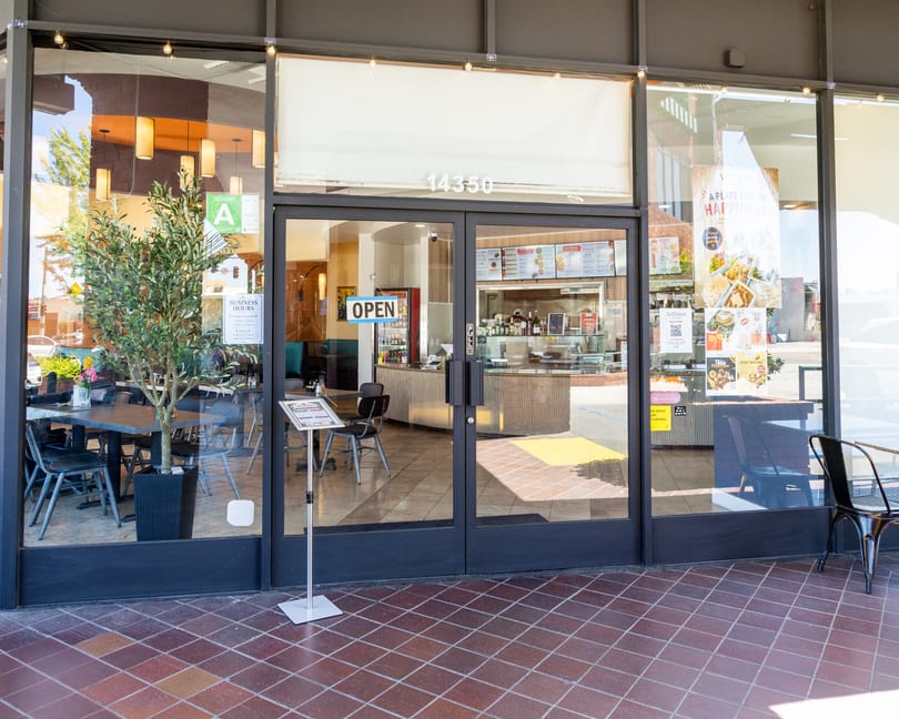 The storefront of Aromas restaurant, with an "OPEN" sign on the glass door and outdoor seating.