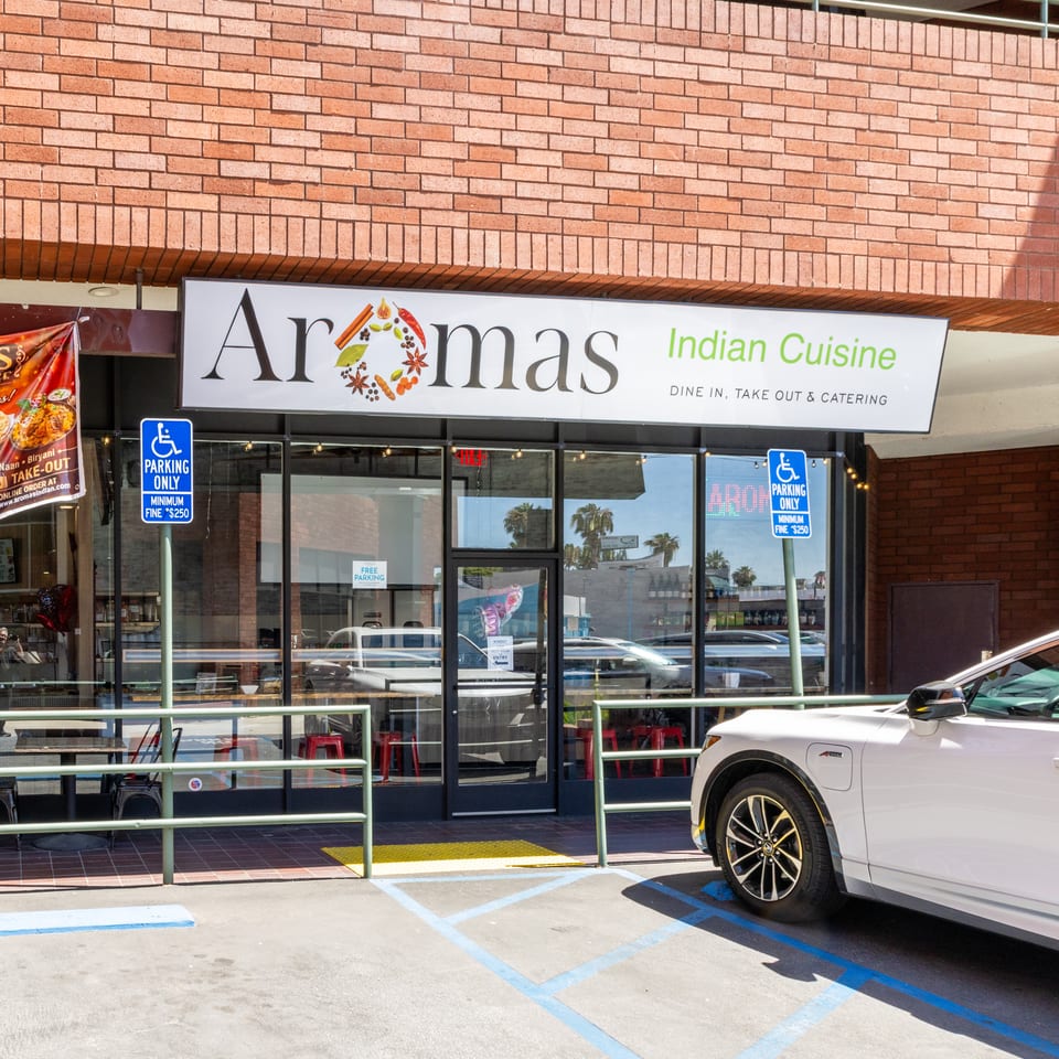 Exterior of Aromas Indian Cuisine restaurant with a white car parked in front.