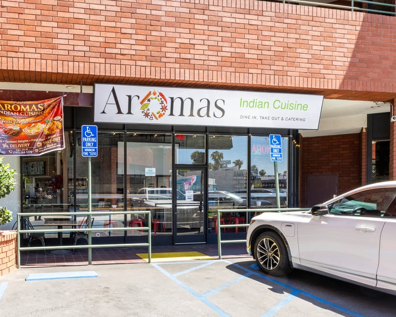 Exterior of Aromas Indian Cuisine restaurant with a white car parked in front.