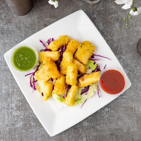 Golden fried paneer pieces on a bed of lettuce and red cabbage, with green and red dipping sauces.