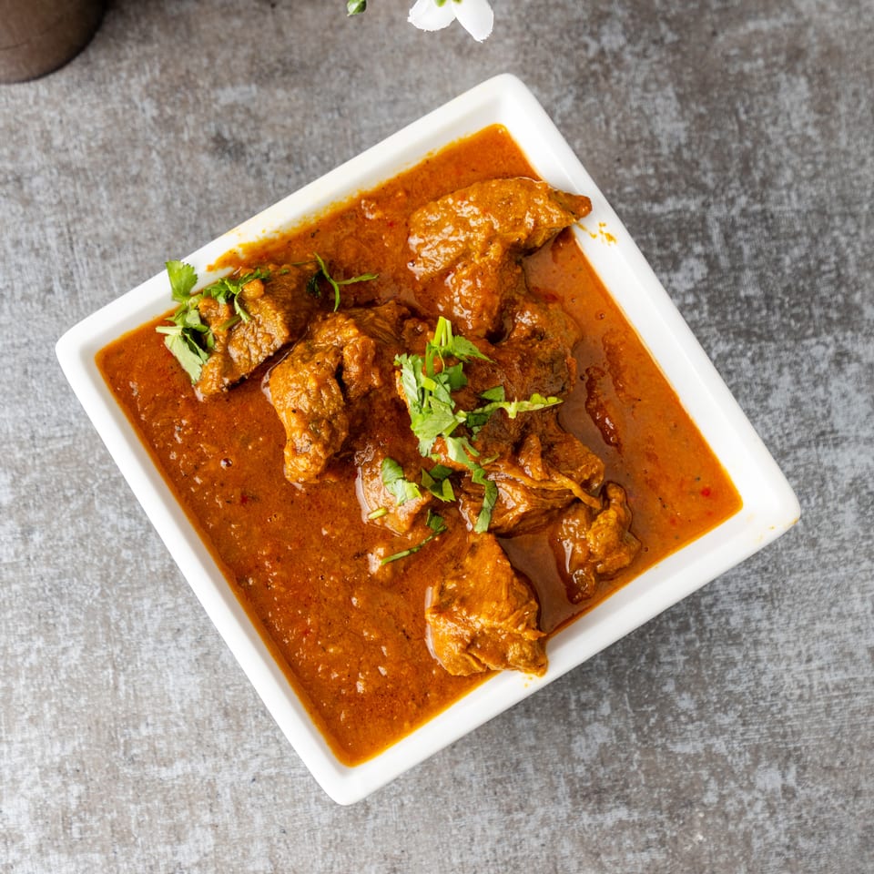 Overhead view of a white rectangular dish filled with a rich, orange-brown curry and meat pieces, garnished with fresh cilantro.