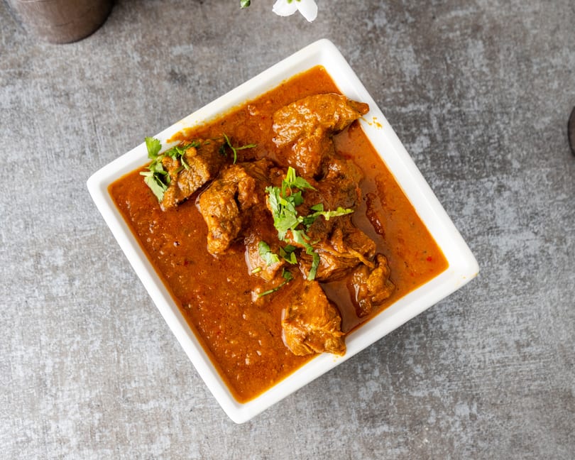 Overhead view of a white rectangular dish filled with a rich, orange-brown curry and meat pieces, garnished with fresh cilantro.