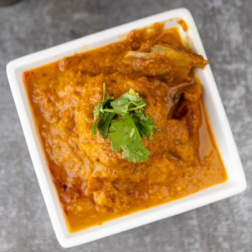 A white rectangular dish filled with a rich orange curry, garnished with fresh green cilantro.