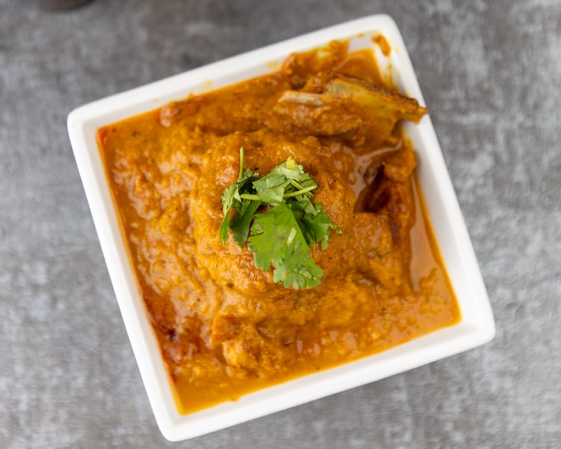 A white rectangular dish filled with a rich orange curry, garnished with fresh green cilantro.