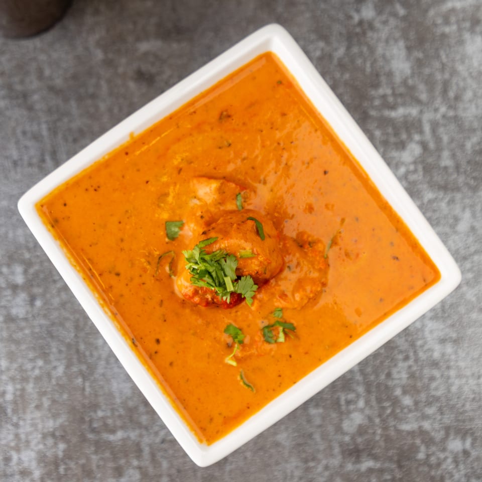 Overhead view of butter chicken in a white square bowl, garnished with fresh cilantro.