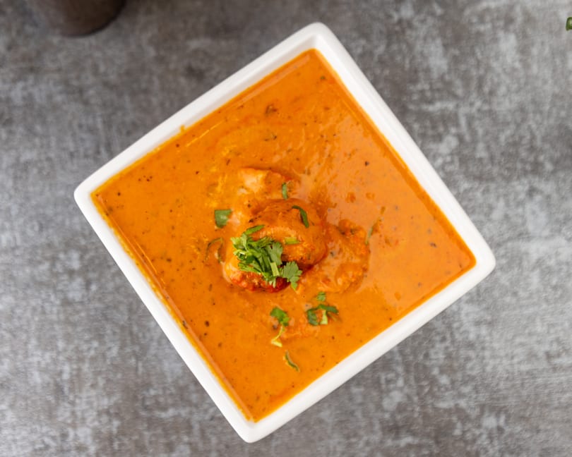 Overhead view of butter chicken in a white square bowl, garnished with fresh cilantro.